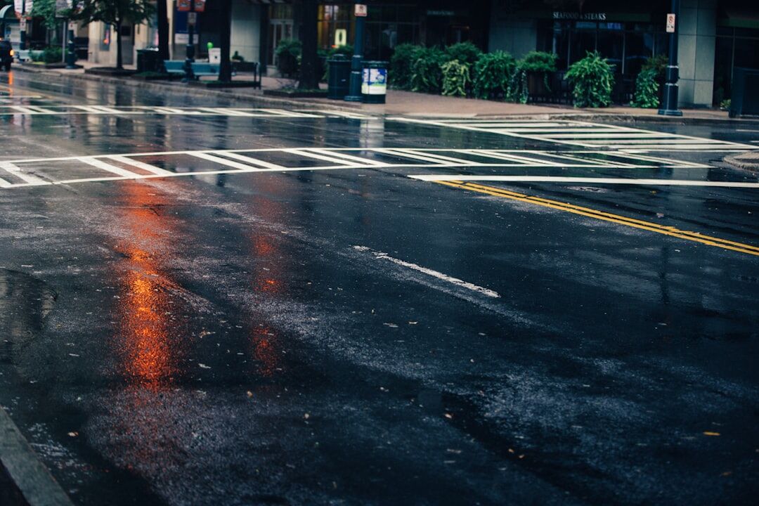 Rainy city street at dusk with blurred lights and wet pavement reflections